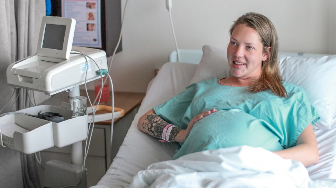 Smiling pregnant woman in hospital bed with her hand on her belly